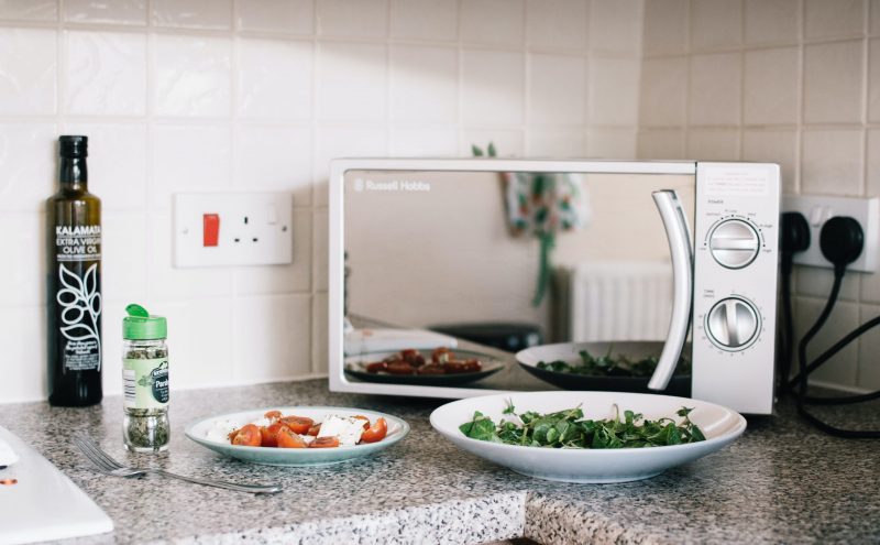 Mikrowelle steht auf einer Küchentheke mit Essen im Vortdergrund