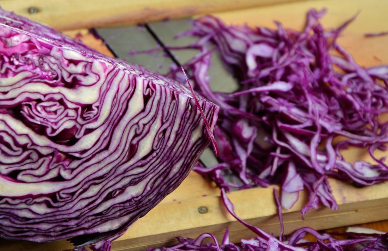 Rotkohl auf einem Küchenhobel aus Holz Mit Küchenhobeln kann Kraut zerkleinert werden