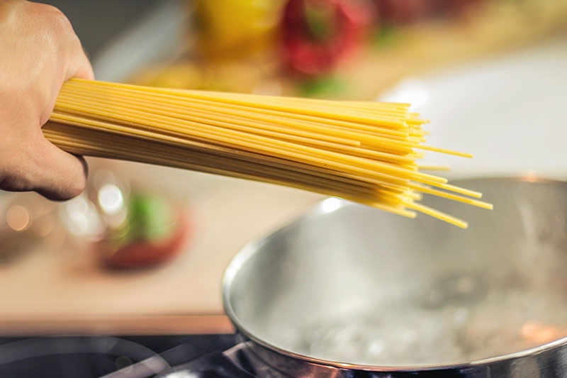 Hand, die Spaghetti über einen Topf hält Spaghetti und ein Topf