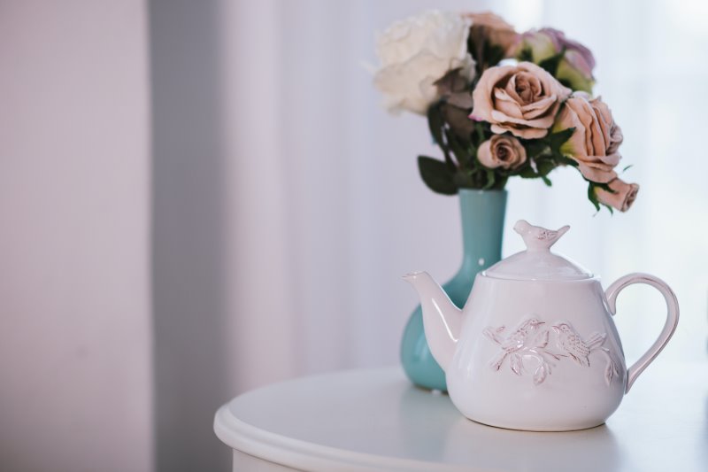 Eine Teekanne aus Keramik mit Blumen Eine weiße Keramik-Teekanne mit Blumen auf einem Tisch