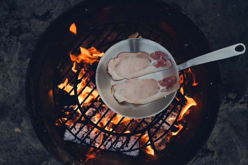 Braten mit handgeschmiedeter Pfanne auf offenem Feuer Fleisch wird in einer handgeschmiedeten Pfanne über dem offenen Feuer gebraten