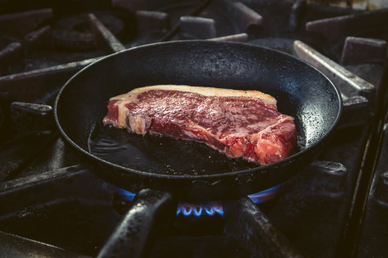 Ein Steak wird in einer handgeschmiedeten Pfanne auf einem Gasherd Steak braten in handgeschmiedeter Pfanne auf einem Gasherd gebraten